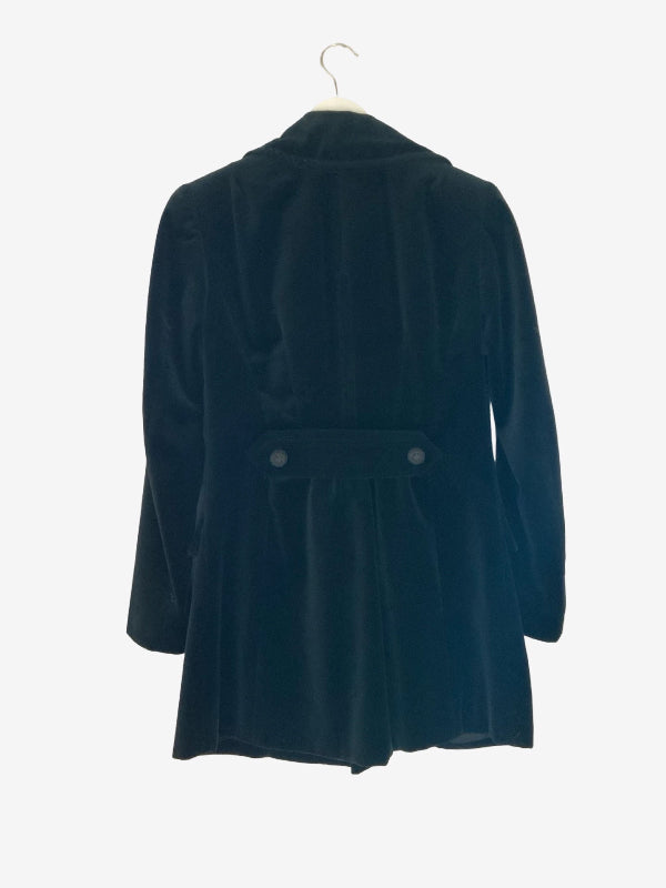 A black velvet longline coat with a pointed collar and a pleated waist, hanging on a white hanger against a plain white background.