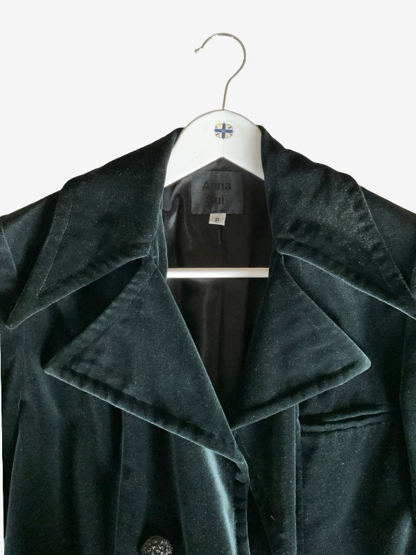 A black velvet coat with wide lapels hanging on a white hanger against a plain white background.