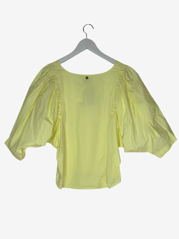 A pale yellow puff-sleeve blouse hanging on a gray hanger against a light gray background.