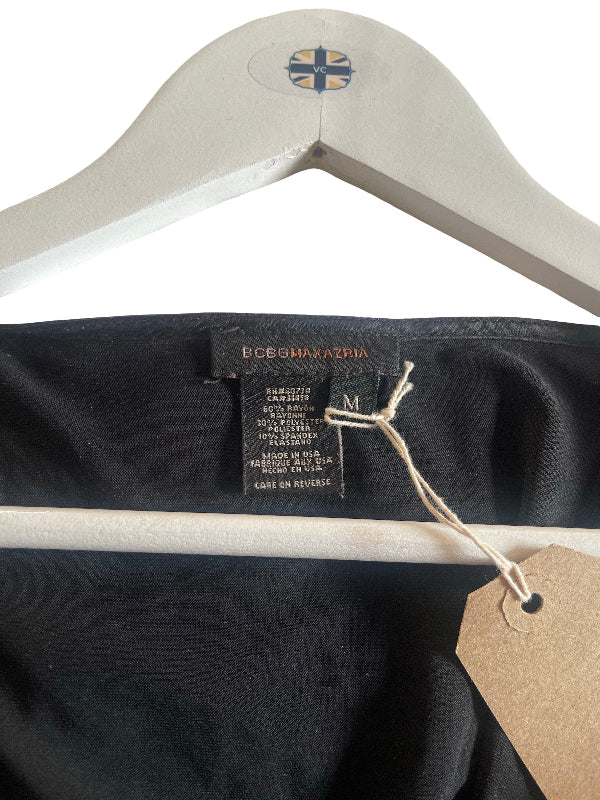 Close-up of a black garment label reading BCBG MAXAZRIA, hanging on a white wooden hanger against a white background.