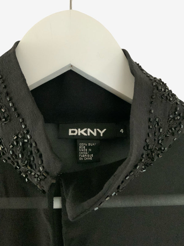 A close-up of a black DKNY blouse on a white hanger, featuring a structured collar embellished with silver rhinestone beadwork.
