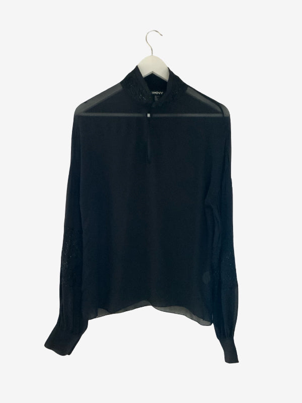 A black long-sleeve blouse with sheer mesh panels and lace detailing on the collar and cuffs, hanging on a white hanger against a light gray background.