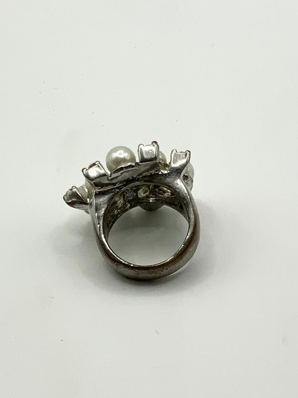 A vintage silver tone ring with a central white pearl and small decorative floral details, shown on a plain light gray background.