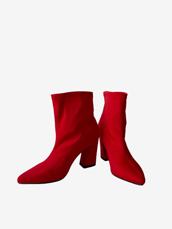 A pair of bright red ankle boots with pointed toes and block heels, shown from the side against a plain light gray background.