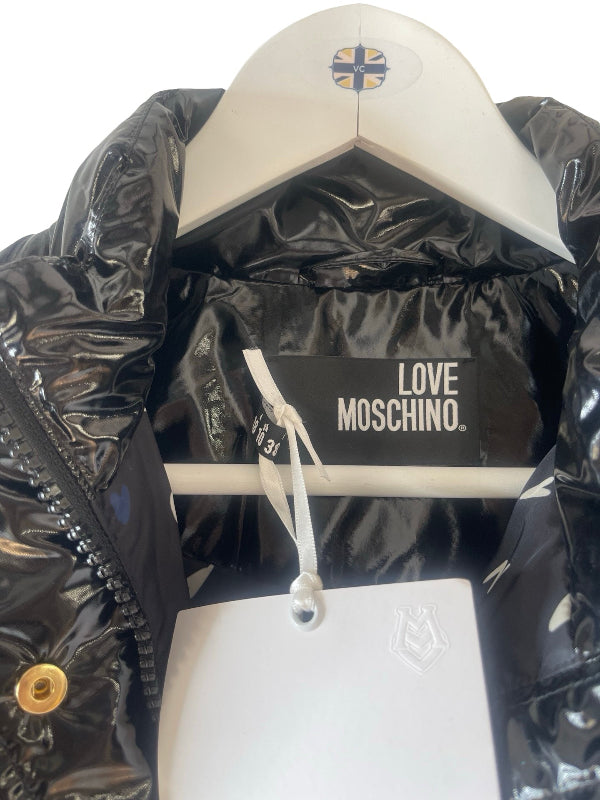 A close-up of a shiny black puffer jacket hanging on a white hanger, with a visible black interior label reading LOVE MOSCHINO. A white hangtag is also attached.
