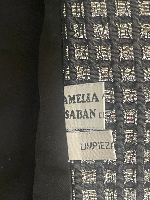Close-up of a black woven fabric with a repeating white monogram pattern and two white sewn-in labels reading 'AMELIA SABAN C' and 'LIMPIEZA Seco - dry clean