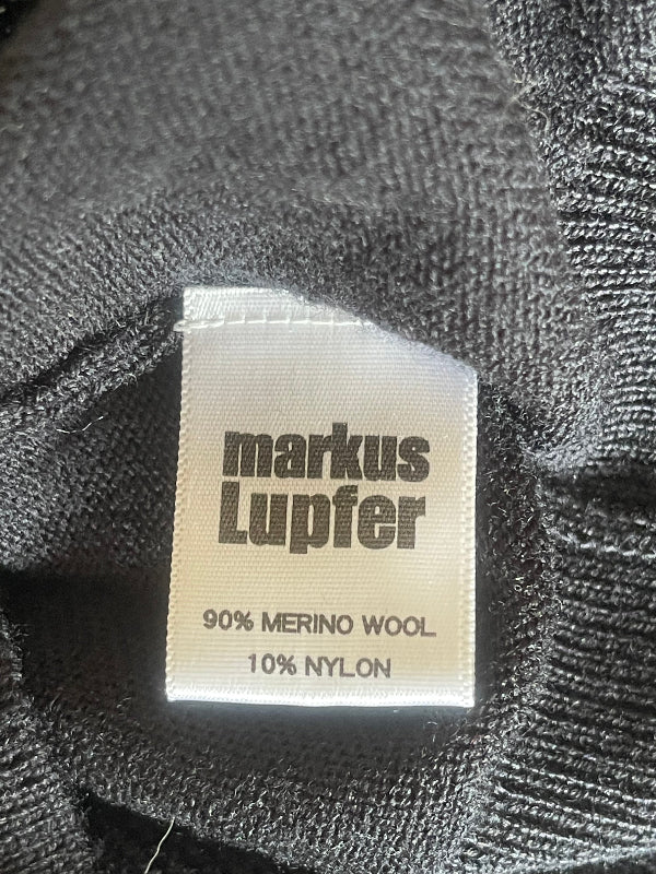 Close-up of a knit garment's interior label reading 'markus Lupfer' with '90% MERINO WOOL 10% NYLON' printed on it.