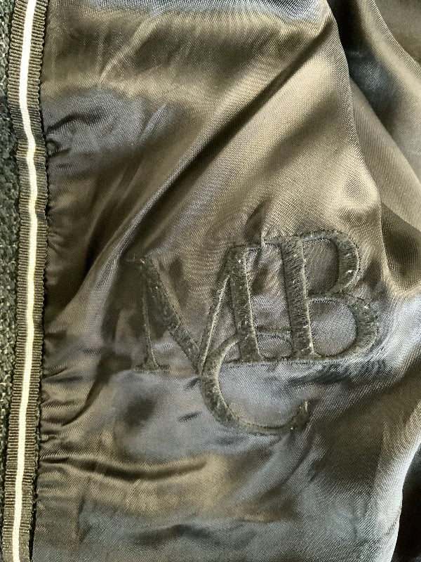 Close-up of a satin or silk-like garment interior in a muted taupe-gray color, with an embroidered monogram reading MB and a striped zipper trim visible along the left edge.