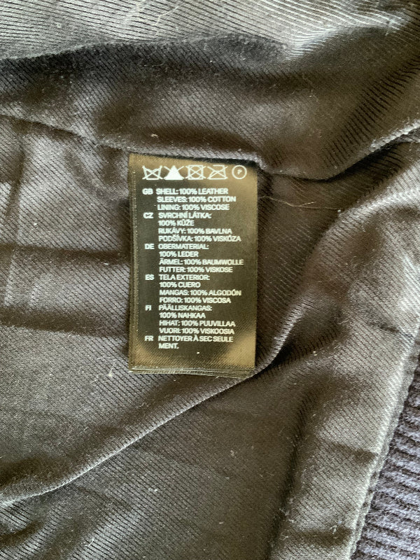 Close-up of a garment's interior label showing material and care information, photographed against dark olive-gray fabric.