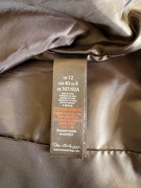 Close-up of a garment's interior neck label sewn onto shiny taupe satin fabric, showing size information and care text.