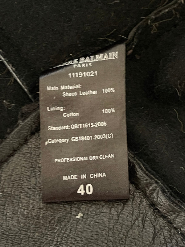 A close-up of a black fabric tag with white text showing details for a Balmain garment, including material, lining, and size 40, set against black leather.