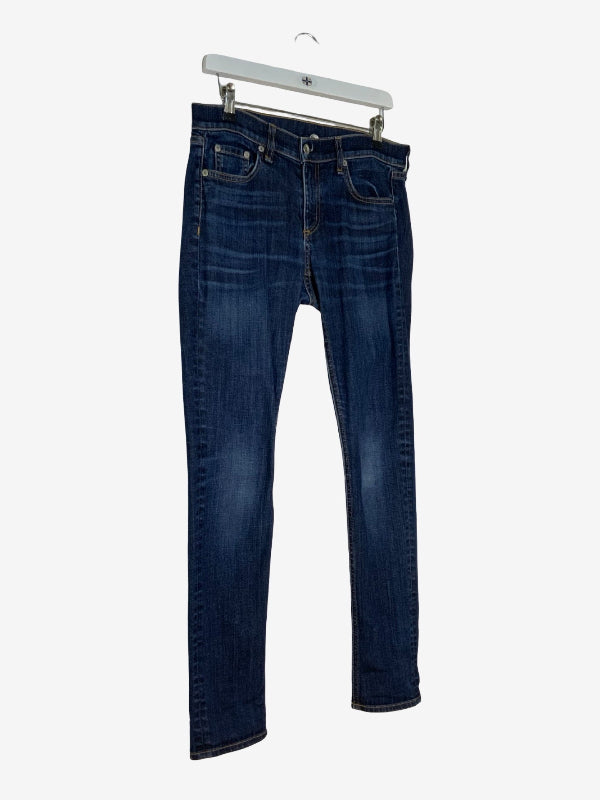 A pair of dark blue slim-fit jeans hanging from a white plastic hanger against a light gray background.
