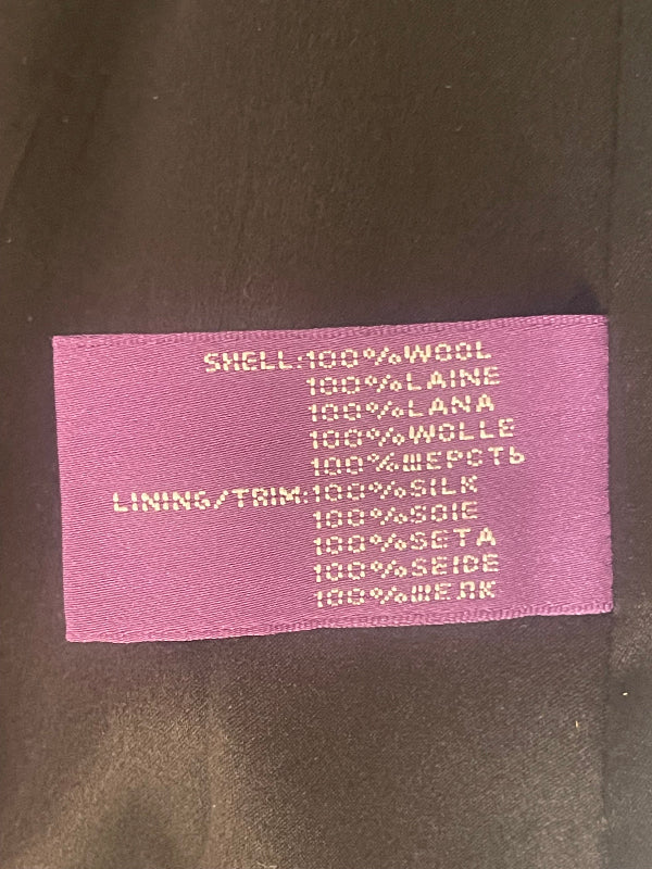 A close-up of a pink fabric care label sewn onto a dark brown garment, showing printed text with material percentages and care instructions.