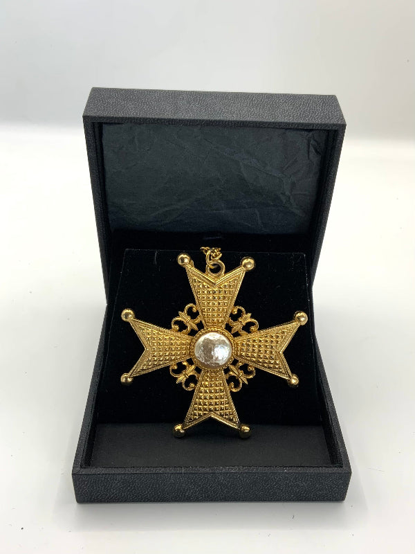 A gold-toned Maltese cross pendant with a central pearl gemstone, displayed inside an open black presentation box on a white background.