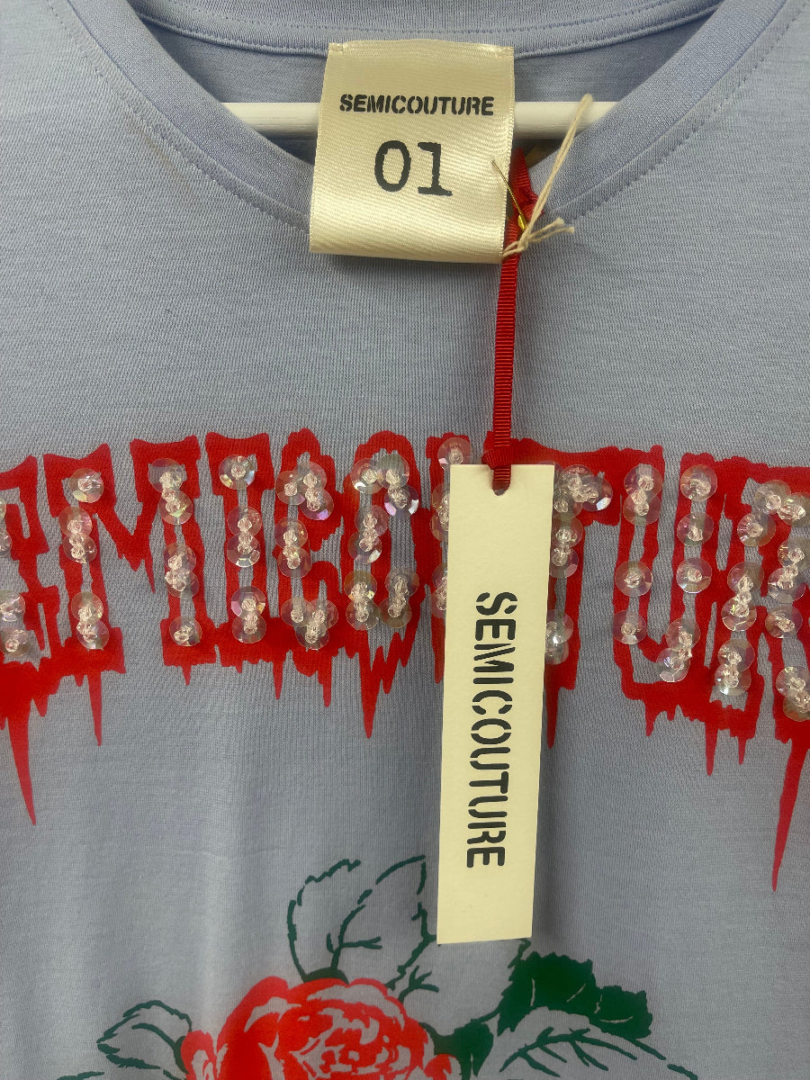 Close-up of a light gray blue Semicouture t-shirt featuring a red graphic text print embellished with clear rhinestones, a red rose, and a paper hangtag.