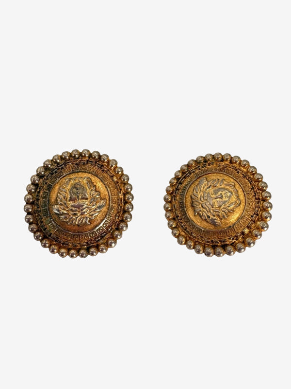 A pair of vintage round gold-toned brooches with intricate floral engravings and beaded borders, displayed on a light gray background.