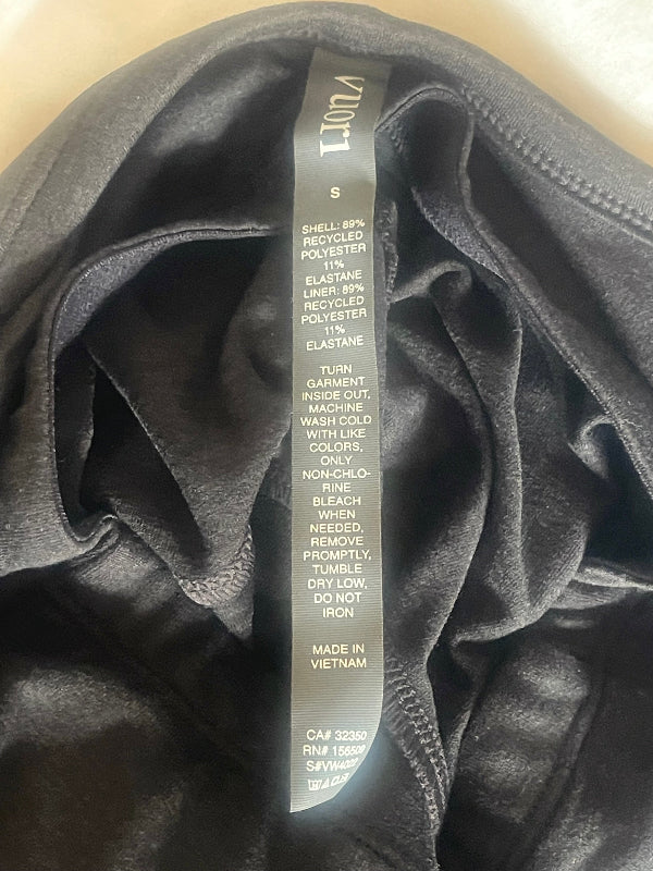 Close-up of a black fabric garment with a sewn-in size and care label reading vuori, shown against a light neutral background.