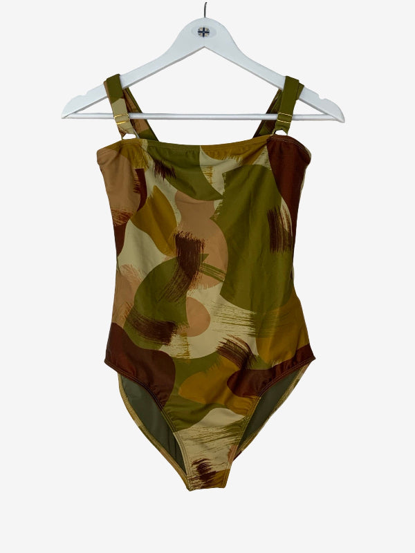 A one-piece swimsuit with a camouflage pattern in olive green, brown, tan, and beige, hanging from a white plastic hanger against a light gray background.