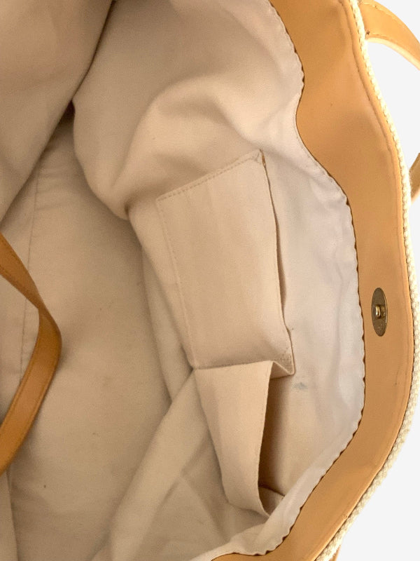 Close-up of the interior of a beige tote bag, showing a cream-colored fabric lining with a side pocket and tan leather trim.