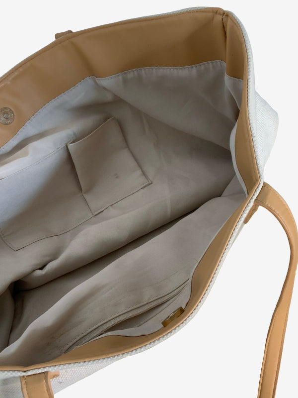 Close-up of the interior of a tote bag, showing a light beige fabric lining, a zippered pocket, and a tan leather strap against a white background.