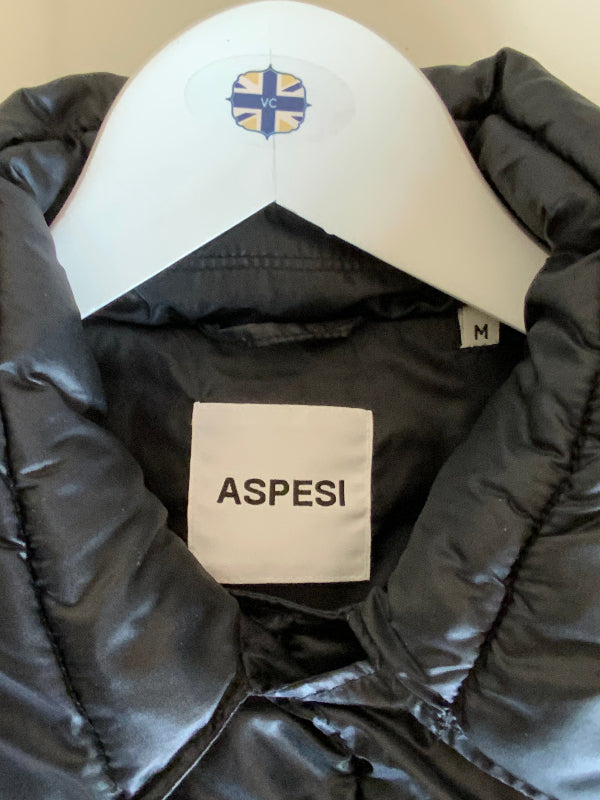 A close-up of a black puffer jacket on a white hanger, showing the interior neck label 'ASPESI' and a small size tag marked 'M'.