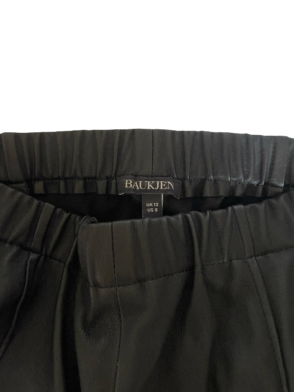 Close-up of the waistband of black pleated trousers by Baukjen, showing the brand label and size details.
