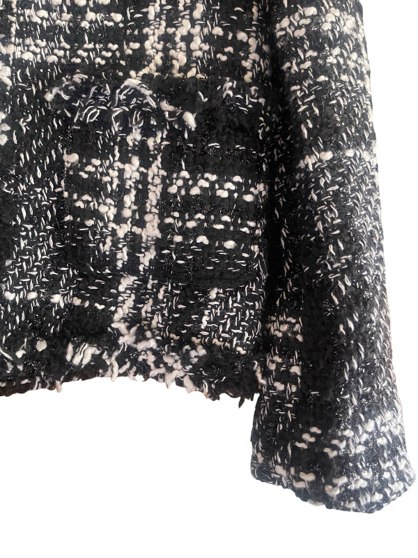 Close-up of a black and white tweed fabric with a textured woven pattern and frayed edges, showing part of a garment sleeve and body against a white background.