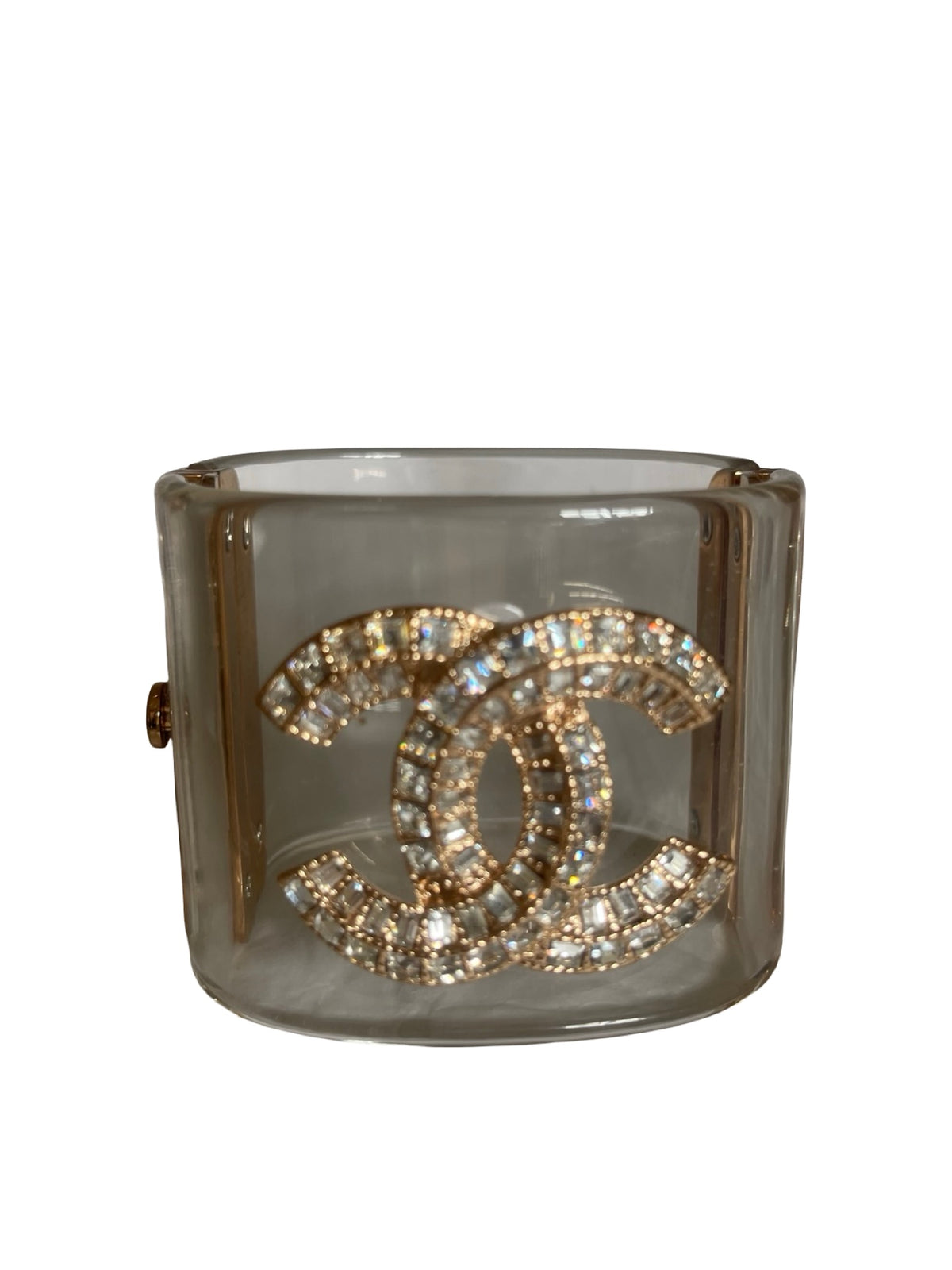 A Chanel cuff bracelet made of clear Perspex translucent with a large gold-tone interlocking CC logo paved with clear crystals, shown on a plain white background.