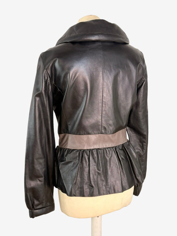 A black leather jacket with a wide collar and a contrasting taupe waist belt, displayed on a beige mannequin torso against a white background.
