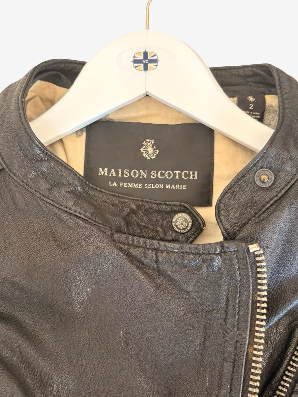 A close-up of a black leather jacket hanging on a white hanger with a Maison Scotch label visible inside the collar.