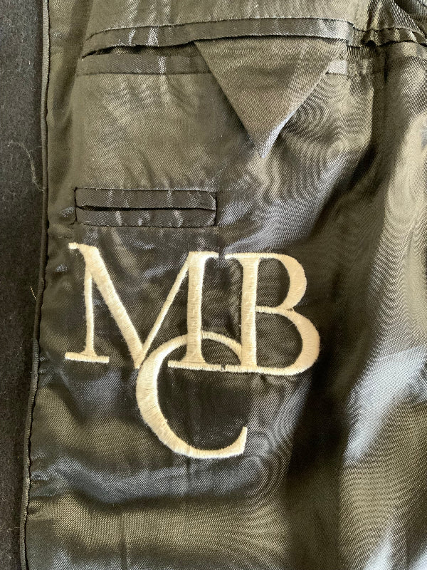 Close-up of a black satin jacket lining with a large cream embroidered monogram reading 'MBC' on the fabric.