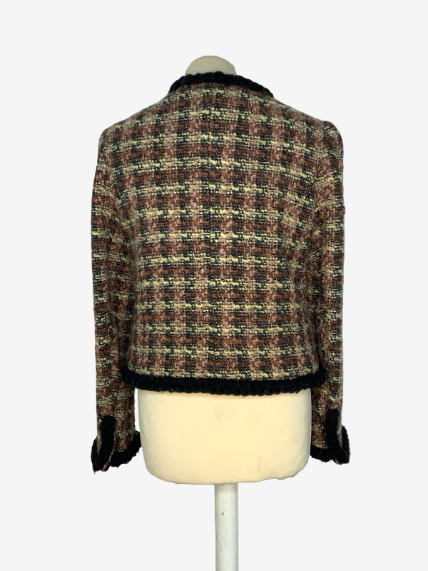 A cropped tweed jacket with a pink, beige, and black plaid pattern, displayed on a cream-colored mannequin torso against a light gray background.