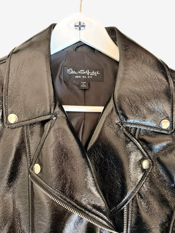 A black faux leather motorcycle jacket with silver-tone snap buttons and a zippered asymmetrical front, hanging on a white hanger against a plain white background.