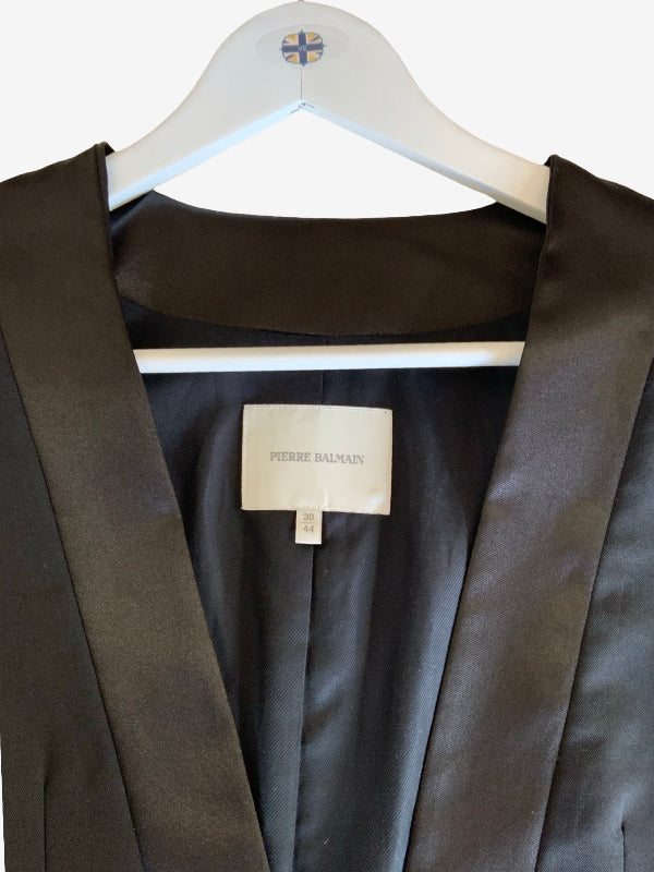 A close-up of a black satin robe jacket hanging on a white hanger with a Pierre Balmain label visible inside the collar.