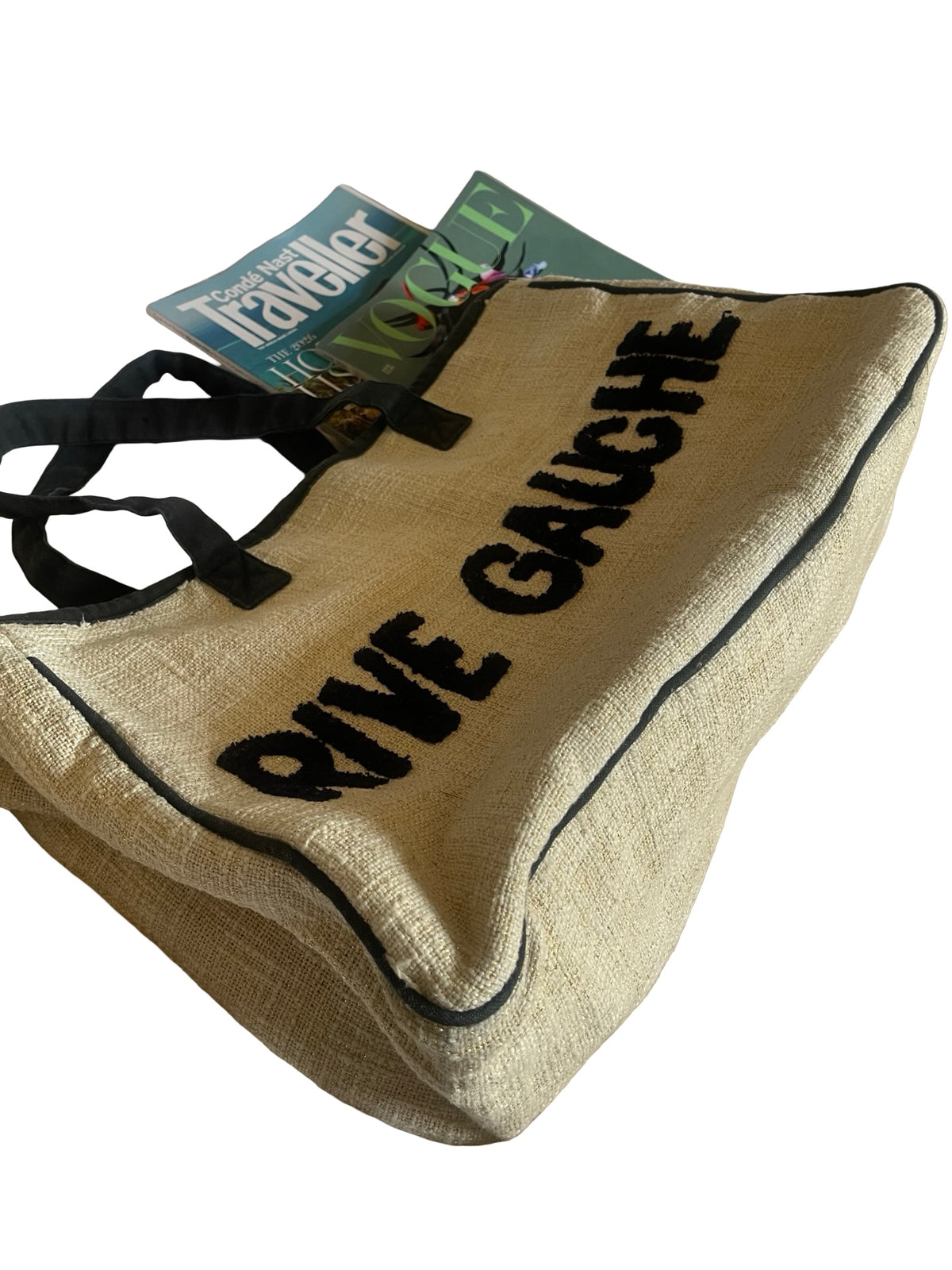 A natural jute tote bag with black trim and black handles, featuring the words 'RIVE GAUCHE' printed in bold black letters. A magazine is tucked inside the bag, which is photographed on a clean white background.