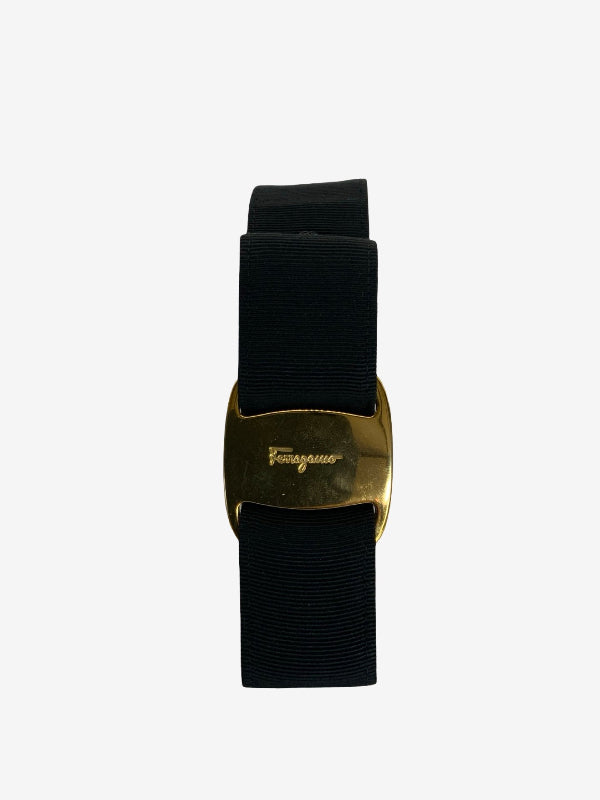 A black woven belt with a polished gold-tone buckle featuring the embossed brand name 'Salvatore Ferragamo', shown against a plain light gray background.