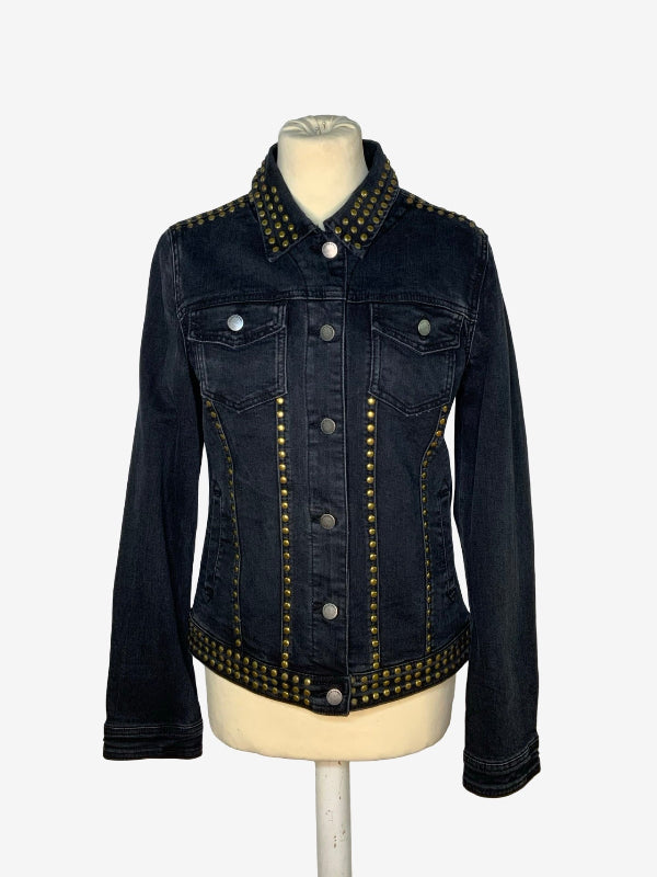 A dark wash denim jacket with gold-tone metal studs, displayed on a cream-colored mannequin torso against a light gray background.