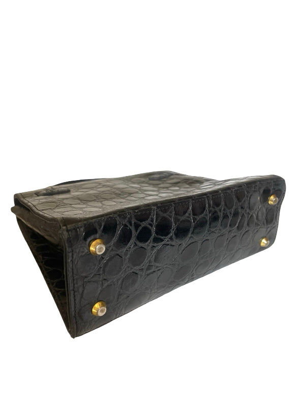 Black crocodile-embossed leather clutch bag with gold-tone metal studs, shown from an angled side view on a white background.