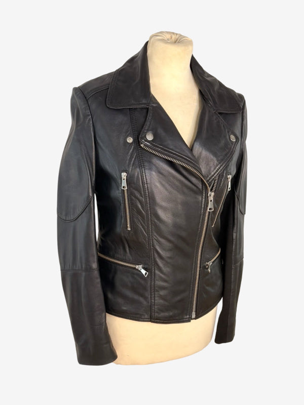 A black leather motorcycle jacket with silver zippers and snap buttons, displayed on a beige mannequin torso against a light gray background.