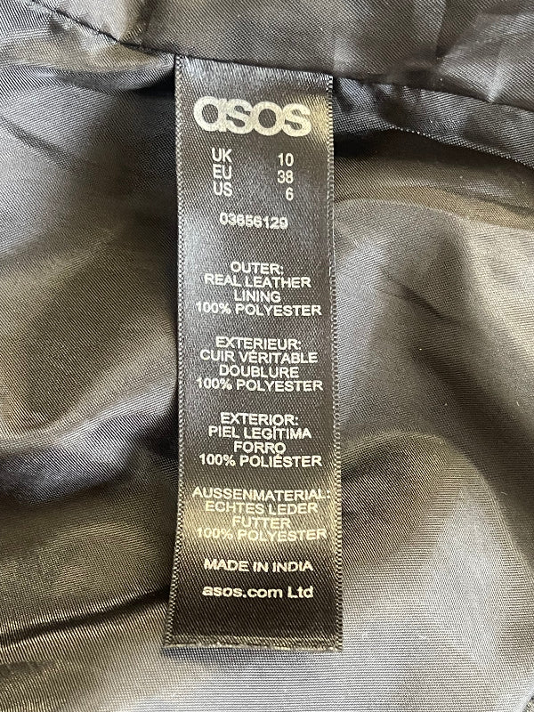 A close-up of ASOS garment interior label sewn onto dark gray or black satin-like fabric. The label shows the Qisos brand name, country code UK, EU 38, US 6, and product details including 'Outer: Real leather lining 100% polyester' and 'Made in India'.