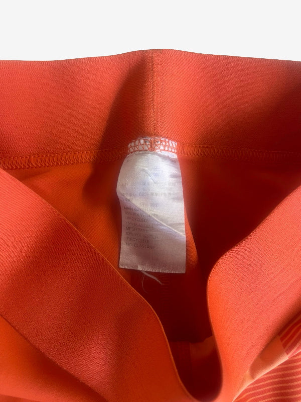 Close-up of a bright orange-red garment interior with a white sewn-in size tag visible at the center, against a light neutral background.