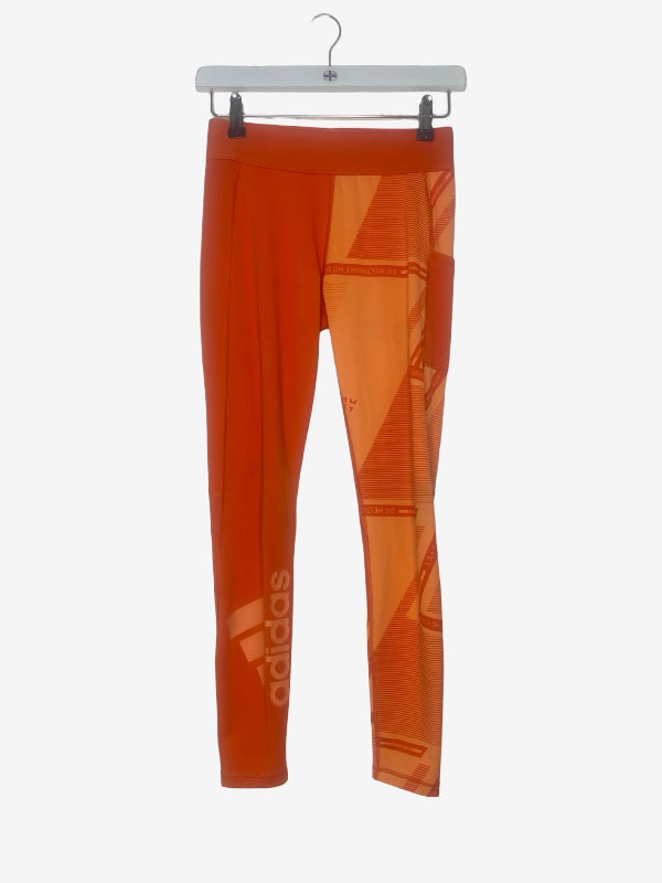 Orange Adidas athletic leggings with a geometric pattern, hanging on a white hanger against a light gray background.