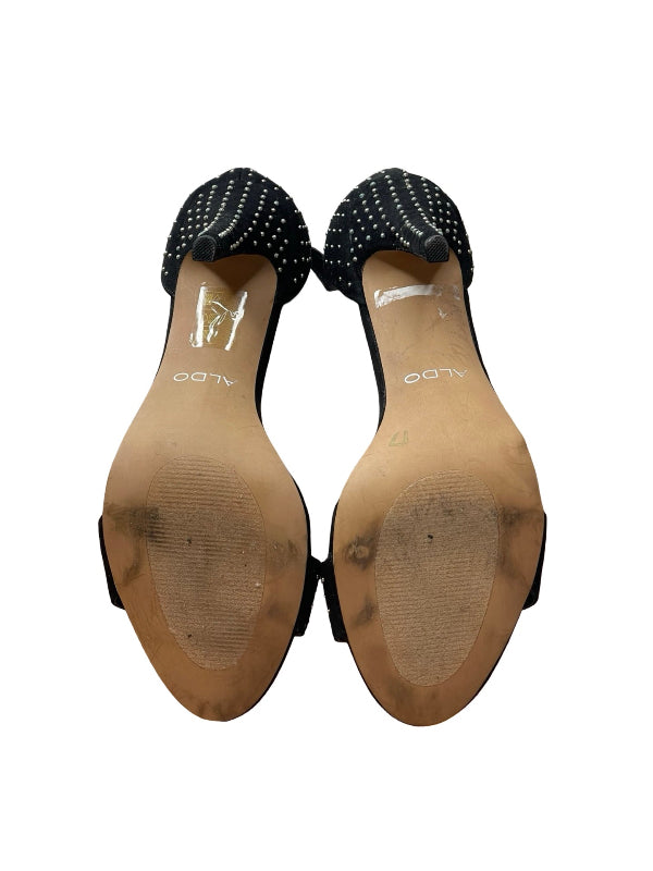 A pair of black pointed-toe heels with white polka dots on the straps, shown from the sole side against a white background. The brand name 'ALDO' is visible on the tan insoles.