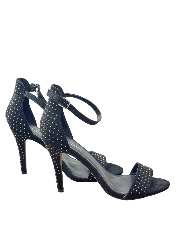 A pair of black studded high-heeled sandals with ankle straps and open toes, shown against a plain white background.