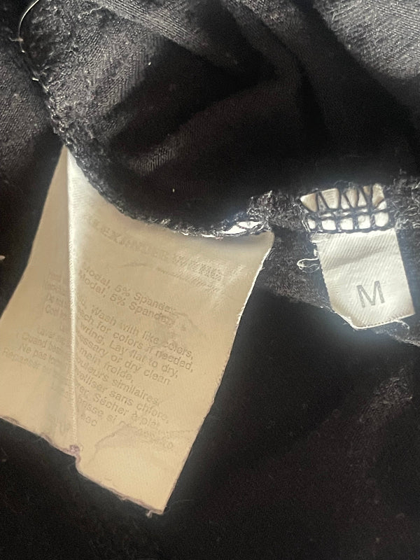 Close-up of the inside neck area of a black garment, showing a white fabric size tag marked 'M' and a sewn paper size label with printed text.