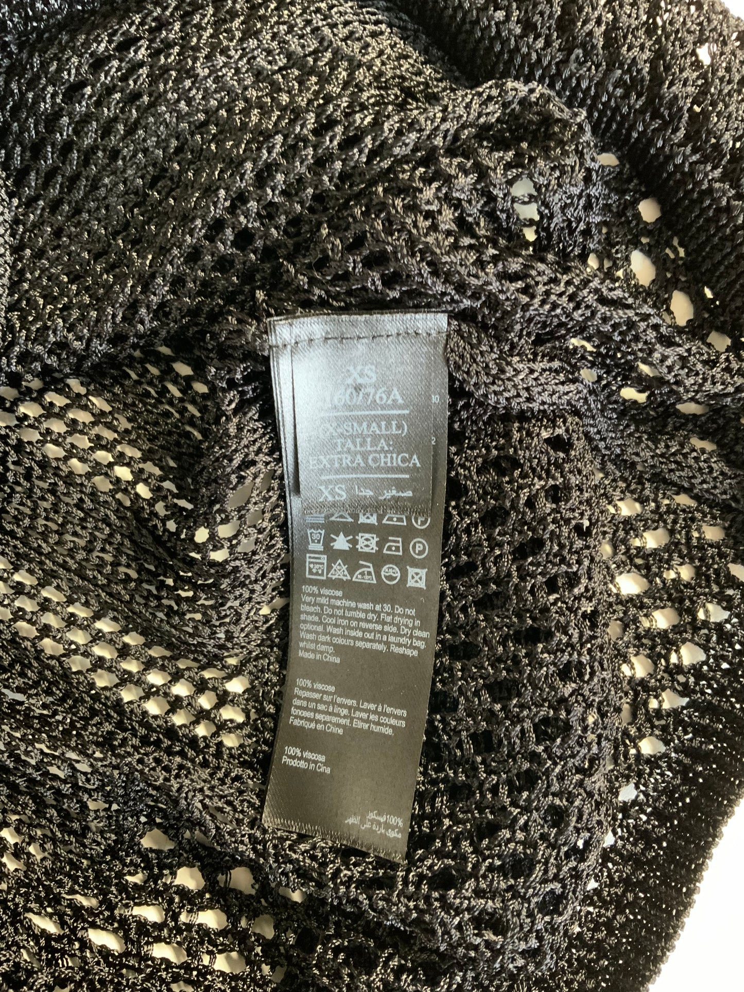 Close-up of a black knit garment label sewn onto a textured black mesh or lace fabric, with the brand name appearing to read Azzaro.