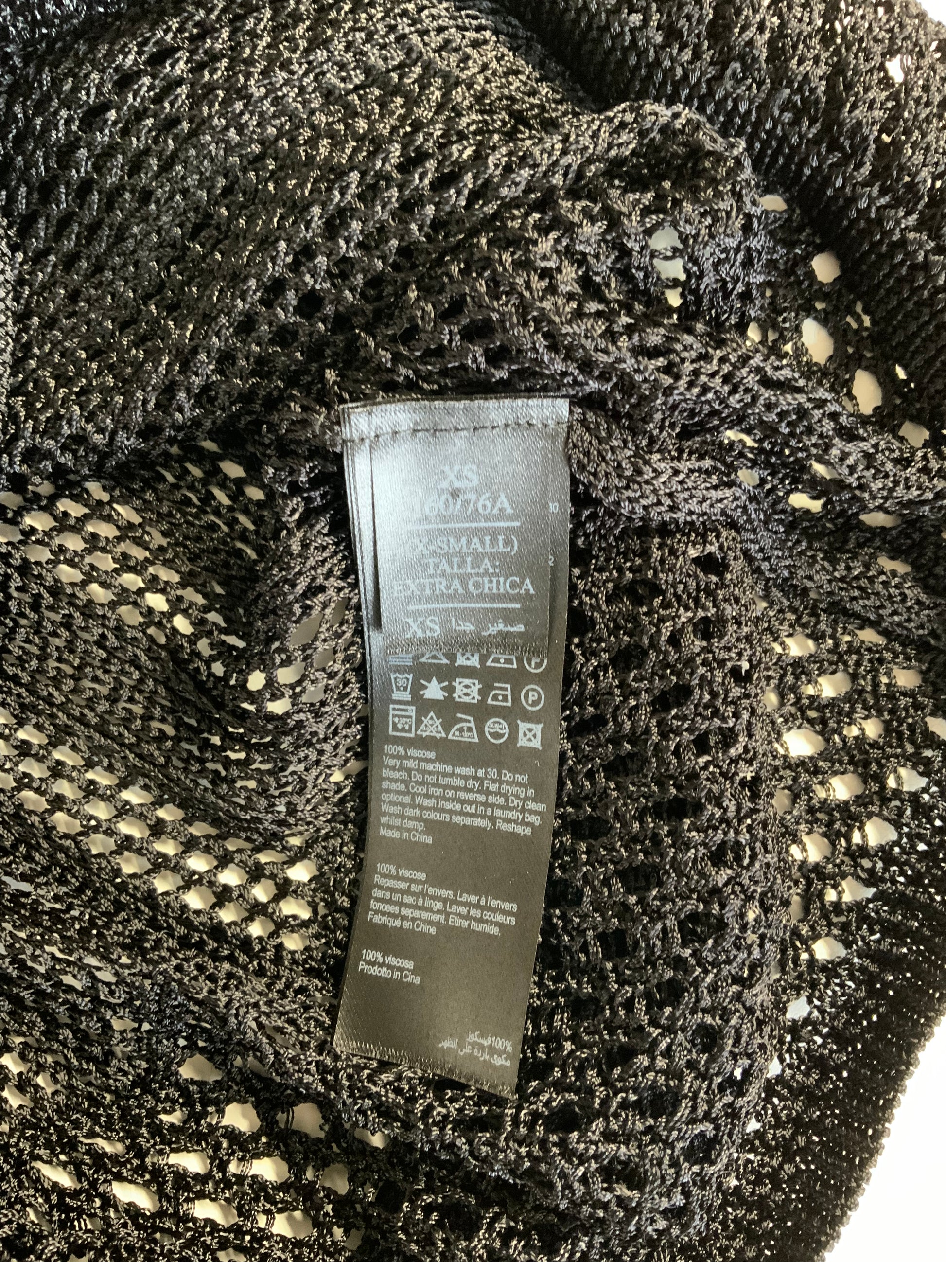 Close-up of a black knit garment label sewn onto a textured black mesh or lace fabric, with the brand name appearing to read Azzaro.