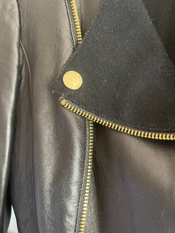 Close-up of a black leather jacket showing a black suede collar with a gold-tone snap button and matching gold zipper.