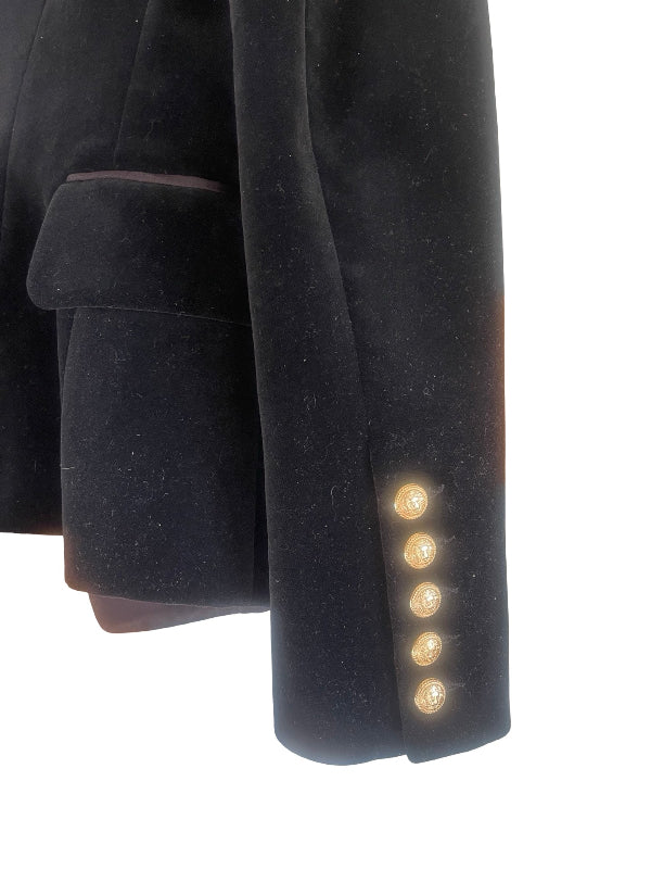 Close-up of a black velvet blazer sleeve showing a row of decorative gold buttons on the cuff, set against a plain white background.