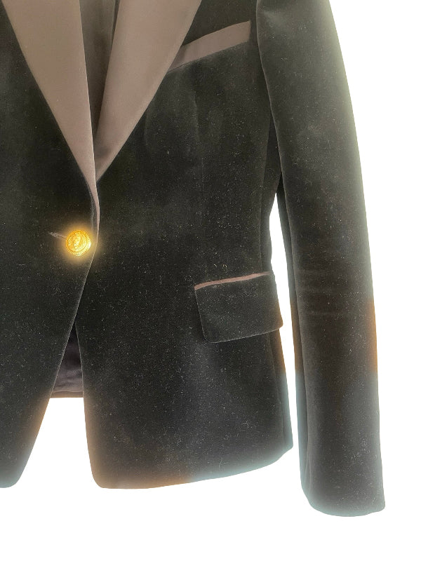 A close-up of a black velvet blazer with a warm beige satin lapel and a single gold button, shown against a white background.